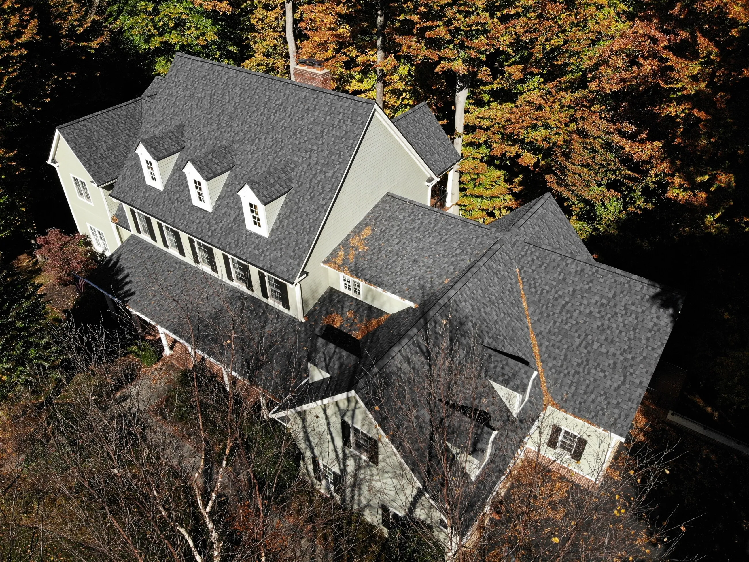 Aerial view of a completed architectural shingle roof surrounded by autumn trees