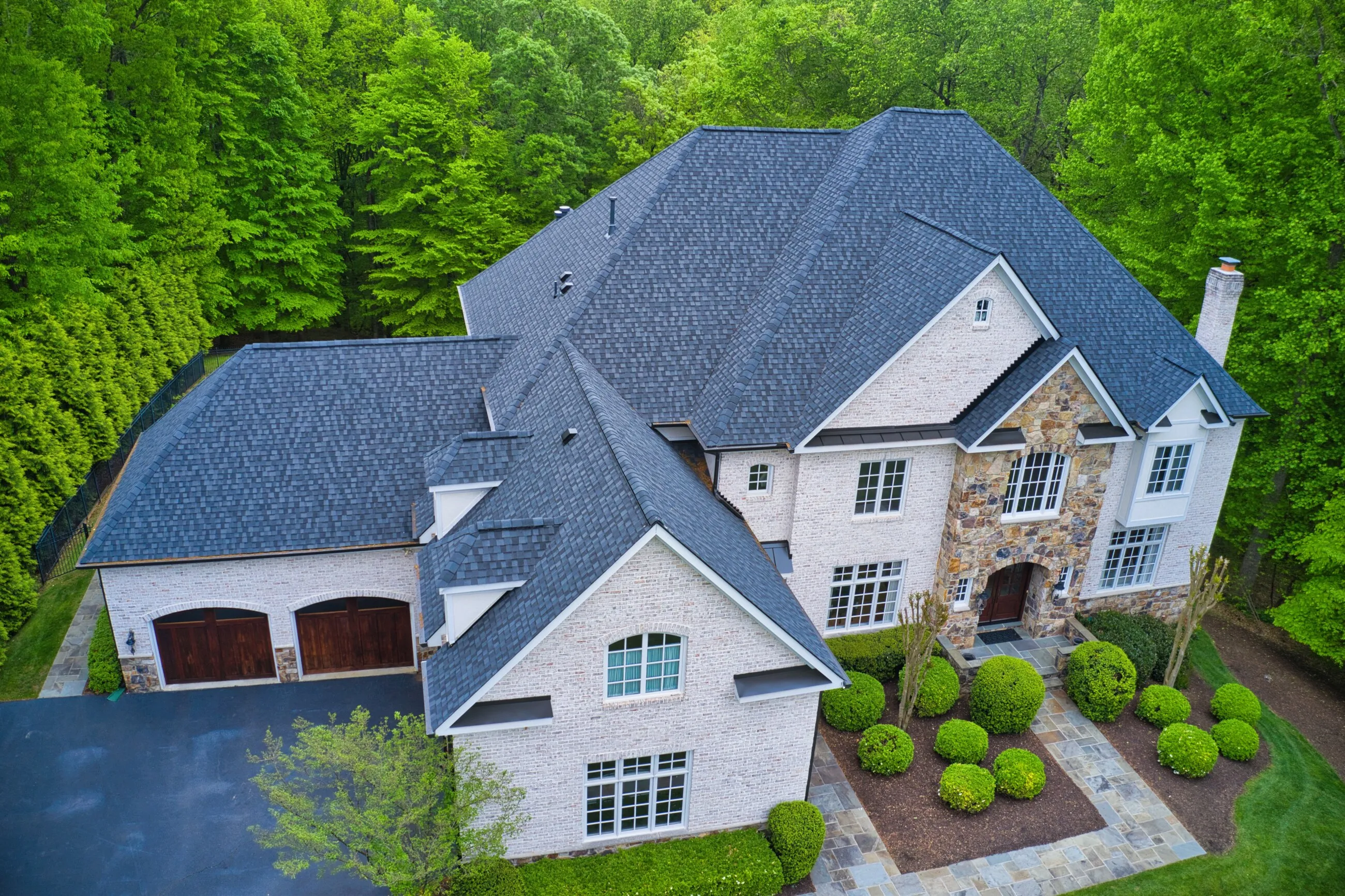 Aerial view of a completed dark shingle roof on a white stone home in Great Falls, Virginia