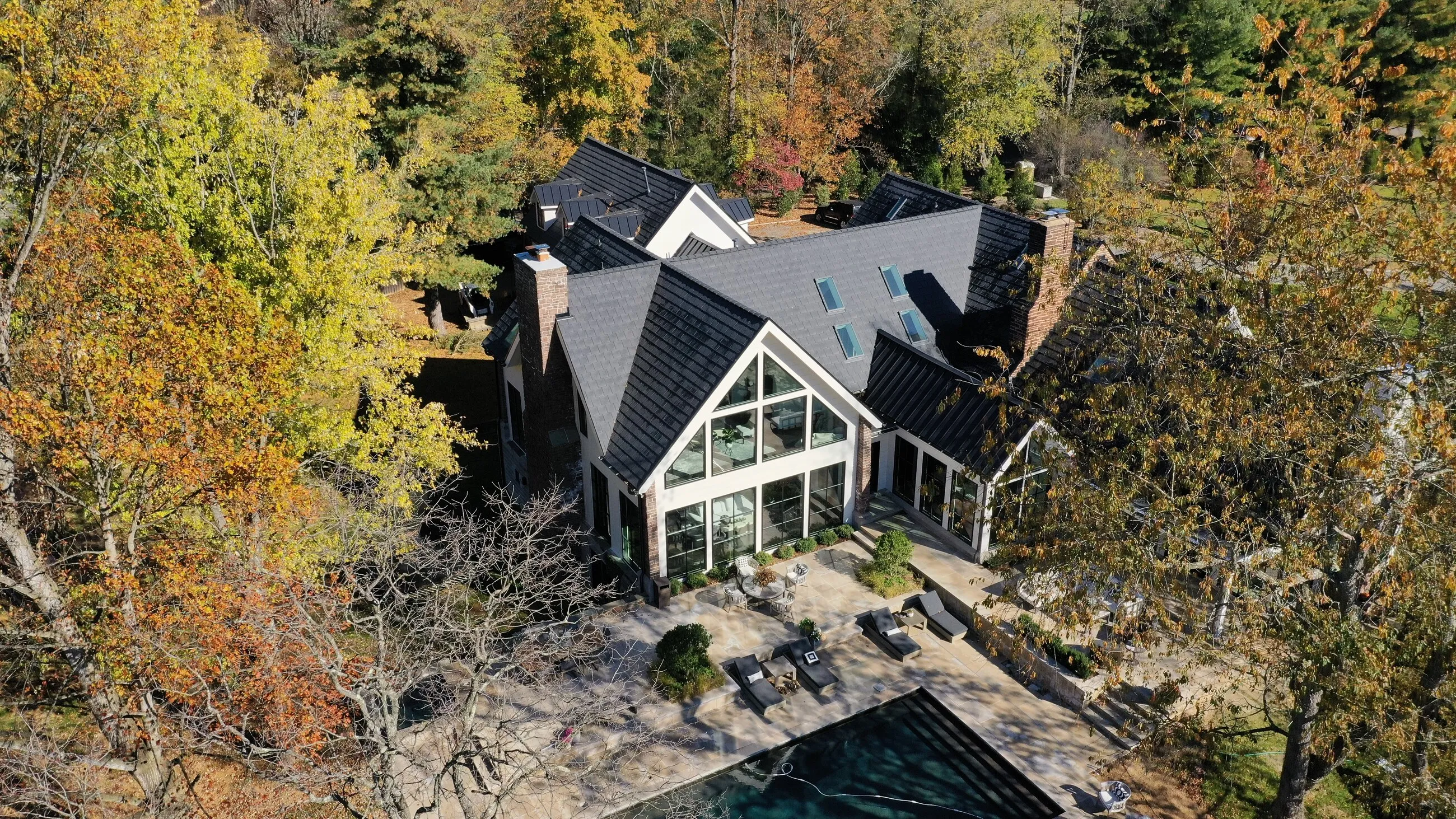 Aerial view of a contemporary home with a new architectural shingle roof beside a pool in autumn