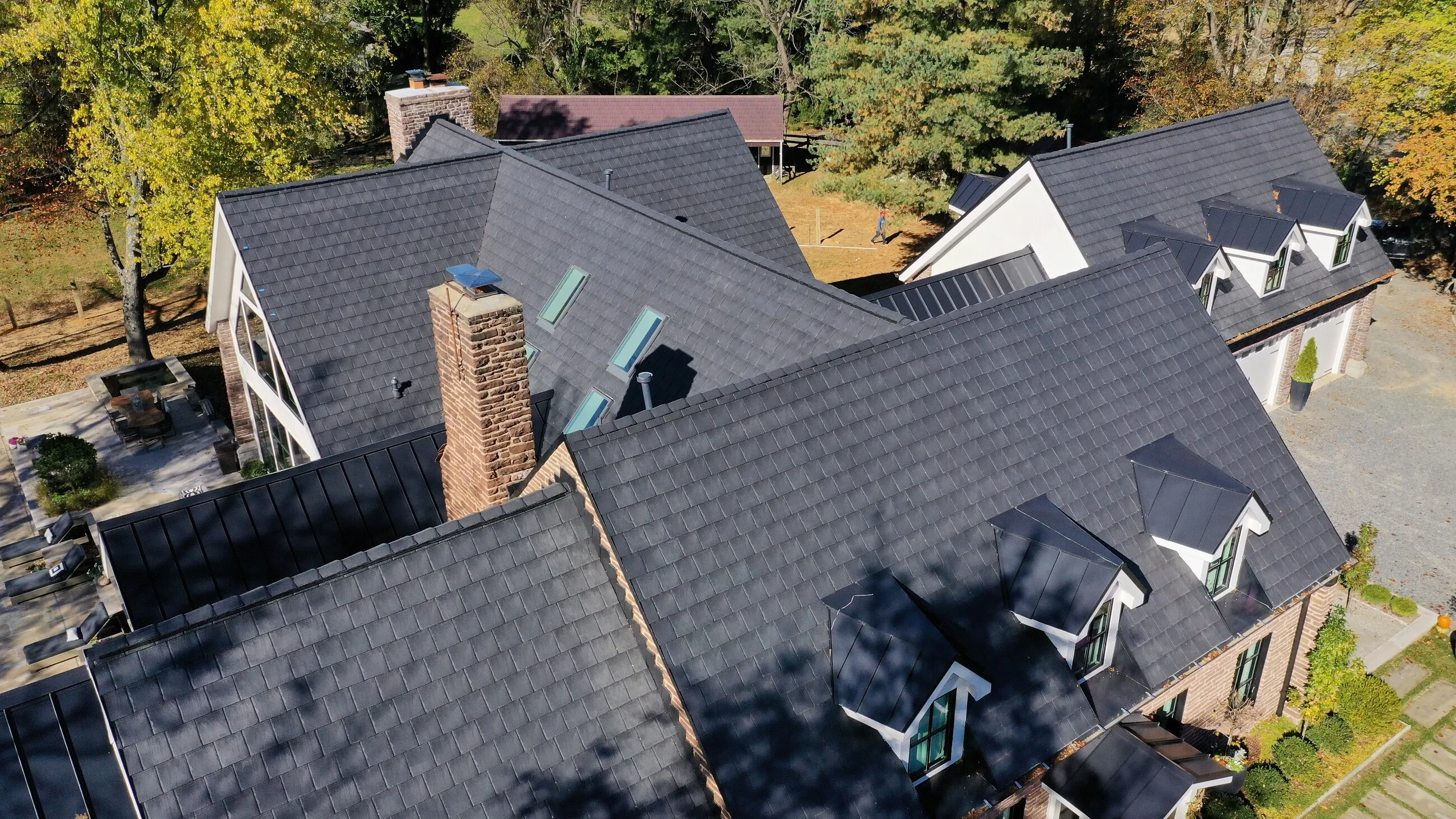 Aerial view of a black slate-style roof with a stone chimney, skylights and standing-seam accents