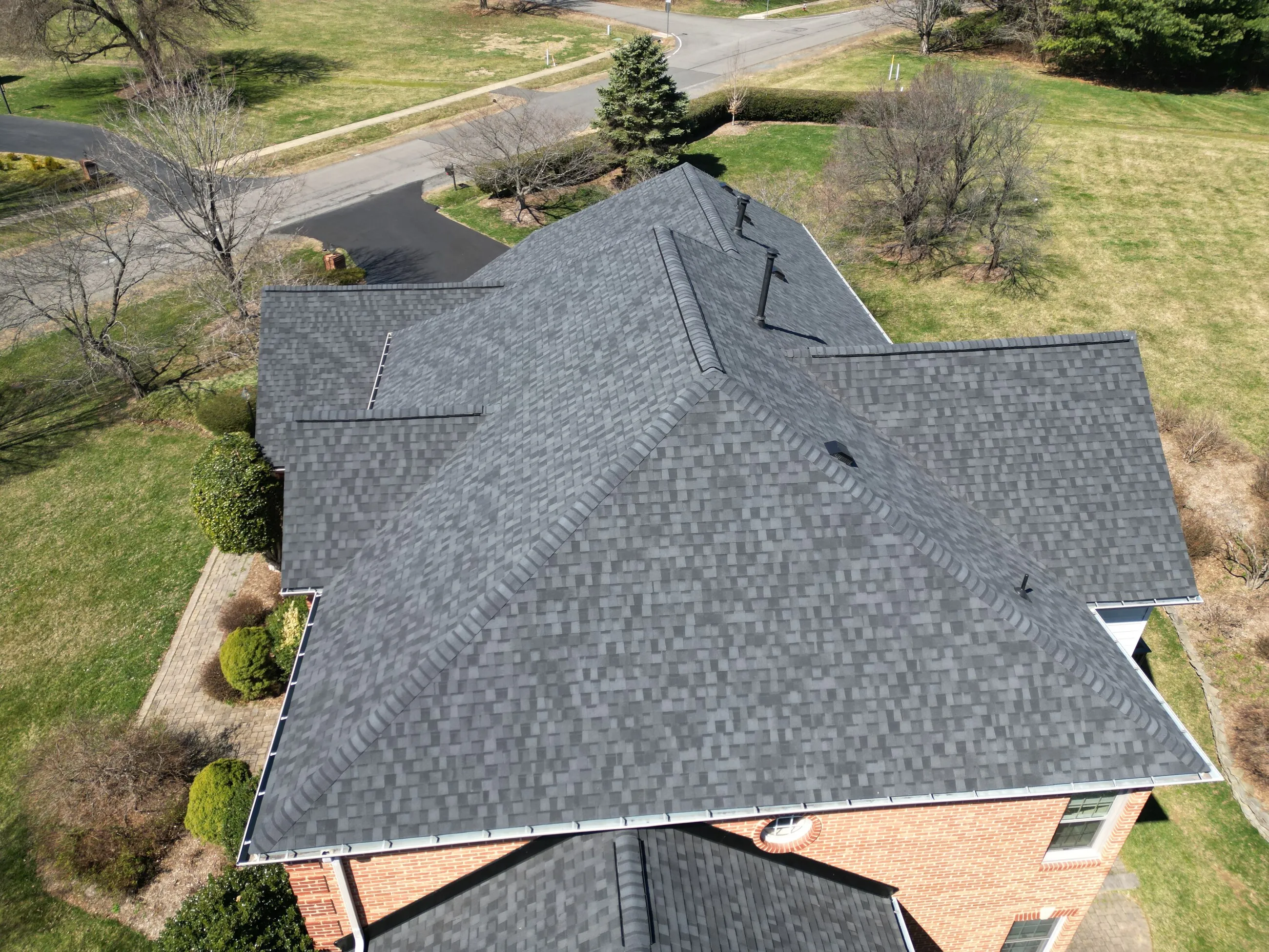 Aerial view of a brick colonial with a new hip roof in early spring