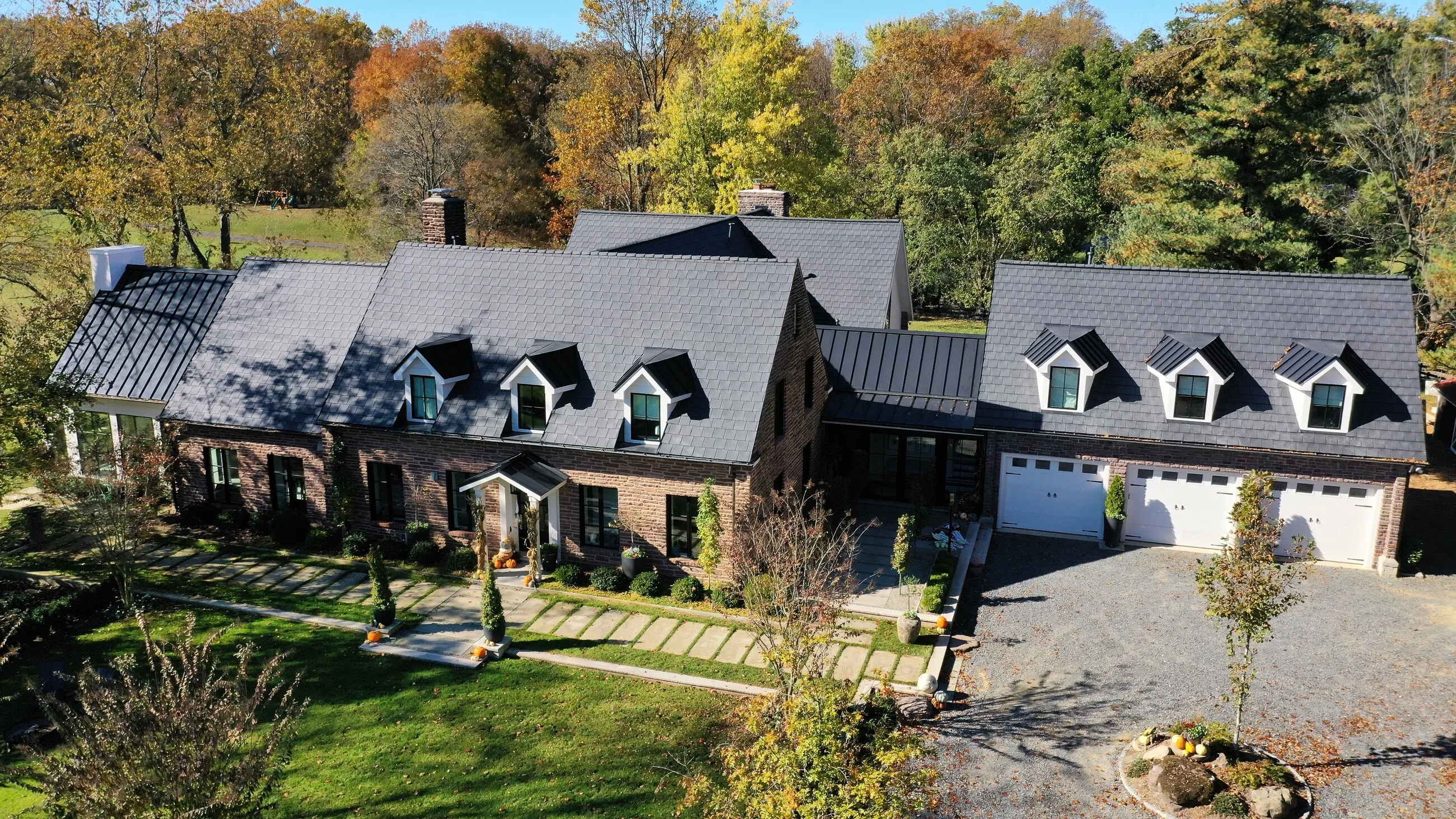 Aerial view of a long brick and stone estate with a new designer shingle roof and standing-seam metal accents in autumn