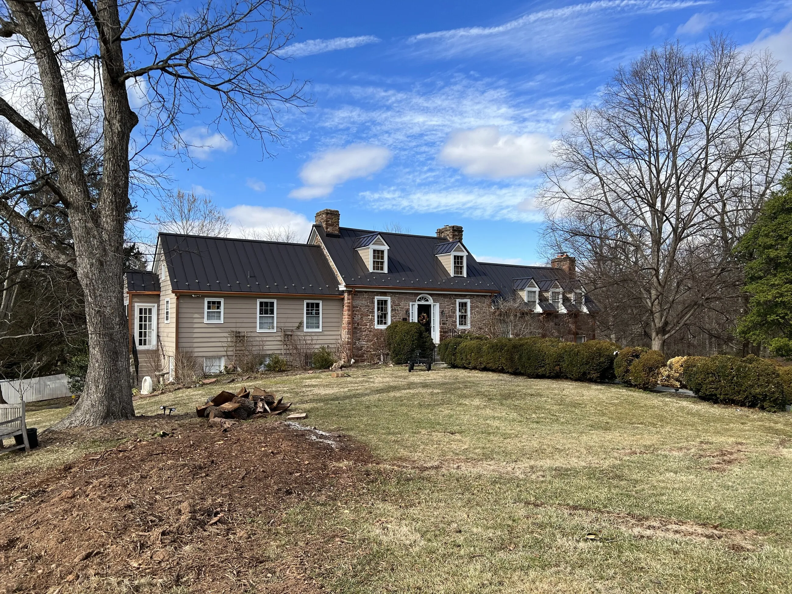 Expanded cape cod home with a black standing-seam metal roof seen across the lawn