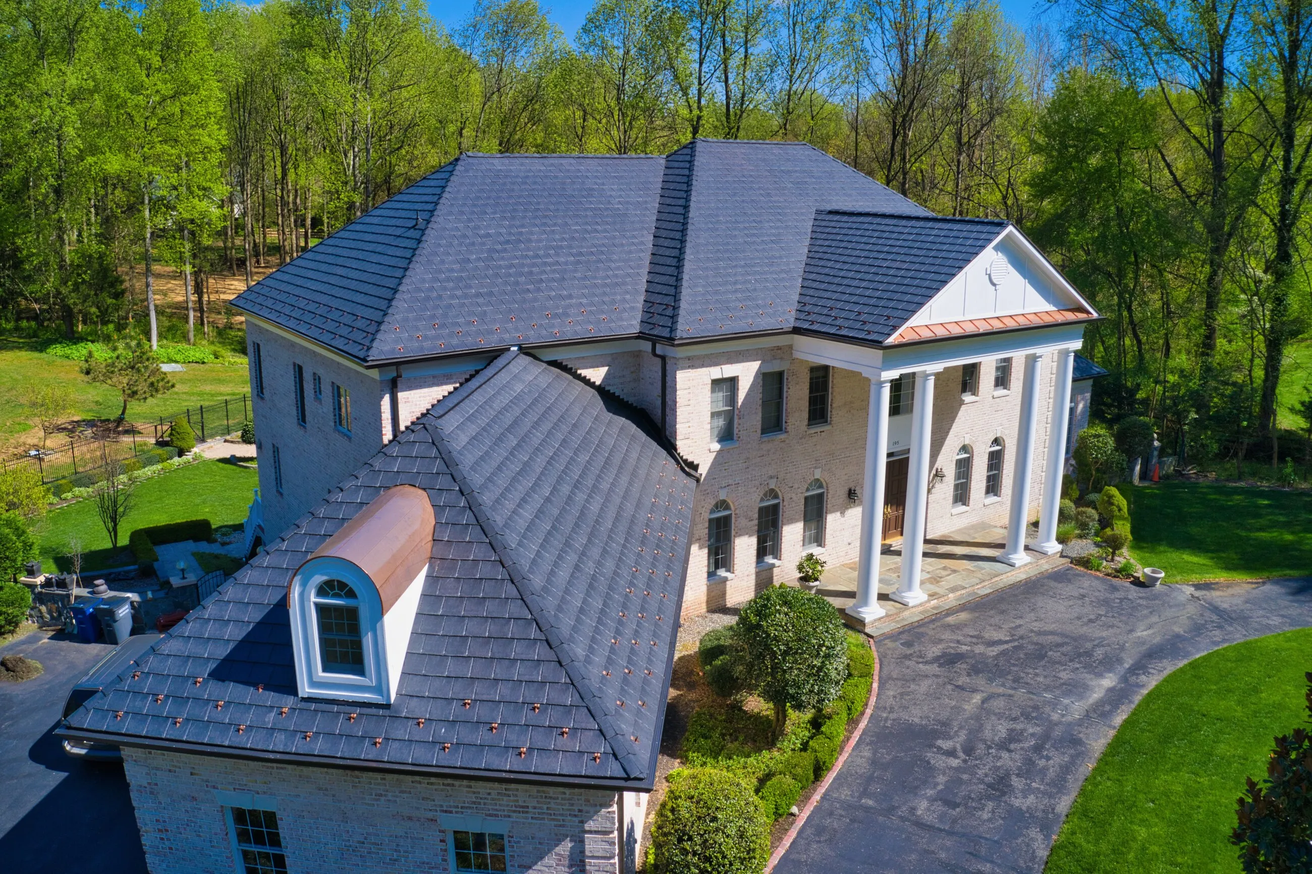 White brick estate with columns, a copper barrel dormer and a new slate-style roof with copper snow guards