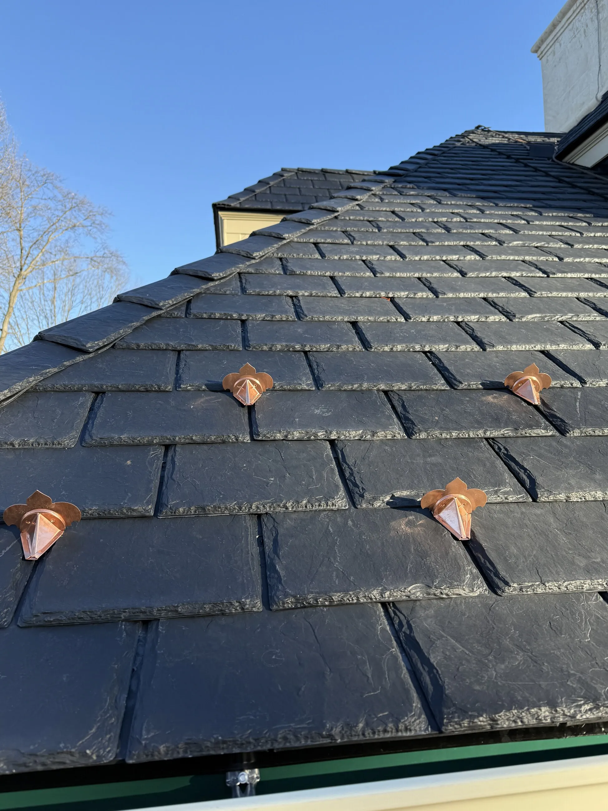 Close-up of black slate roofing with leaf-shaped copper snow guards