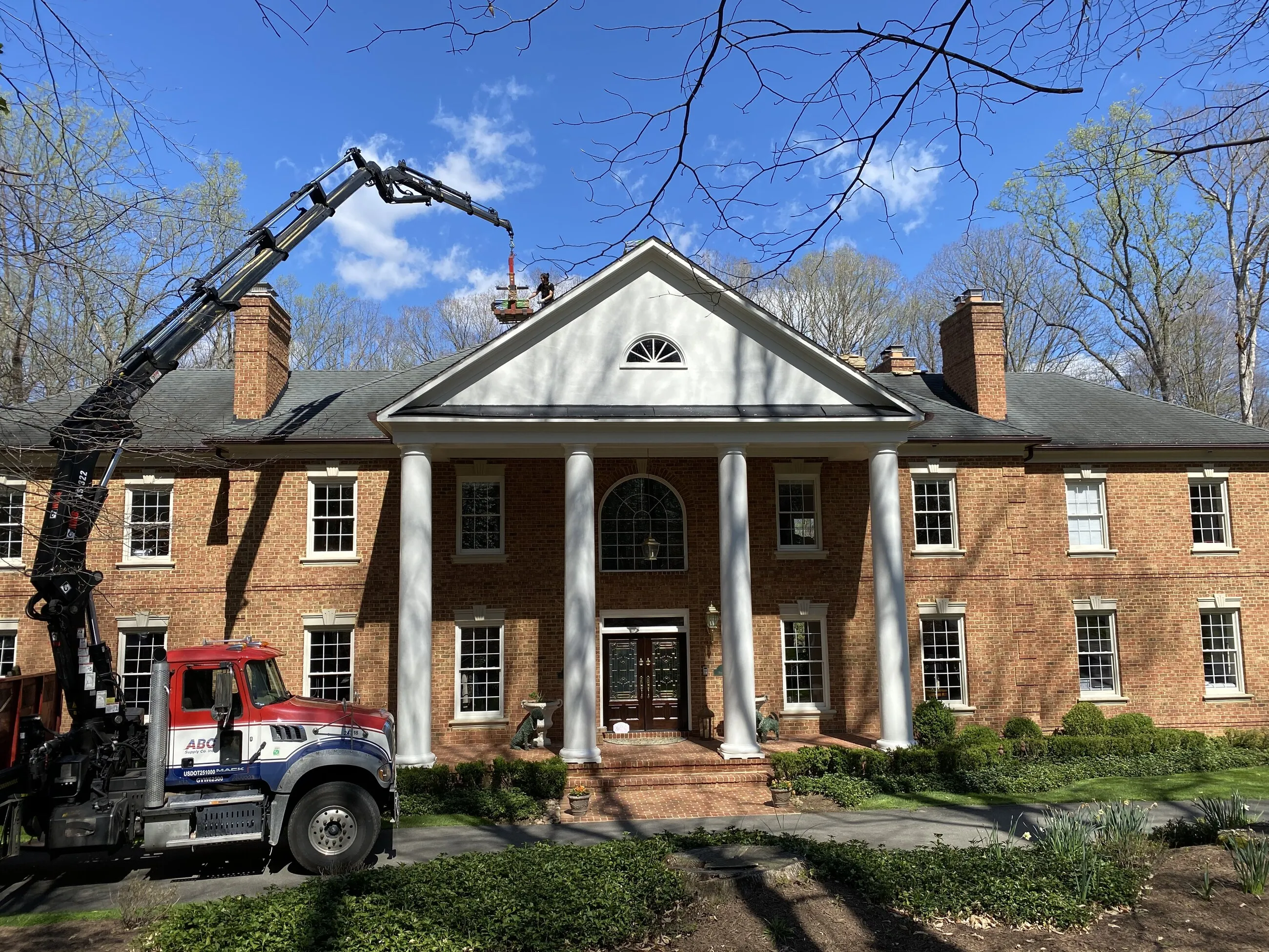 Boom truck delivering roofing materials over the front of a columned brick estate