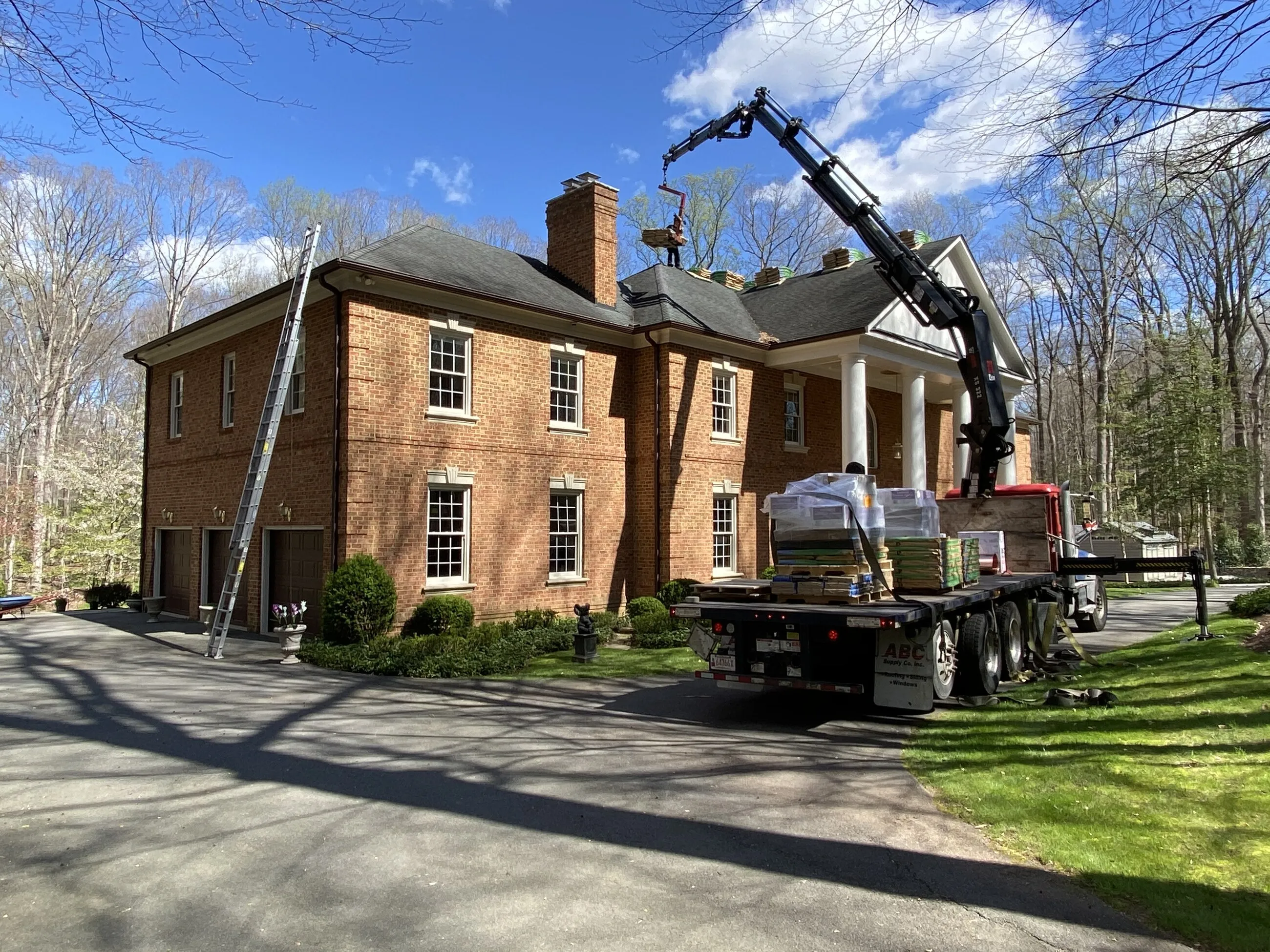 Boom truck lifting roofing materials onto the roof of a brick colonial home