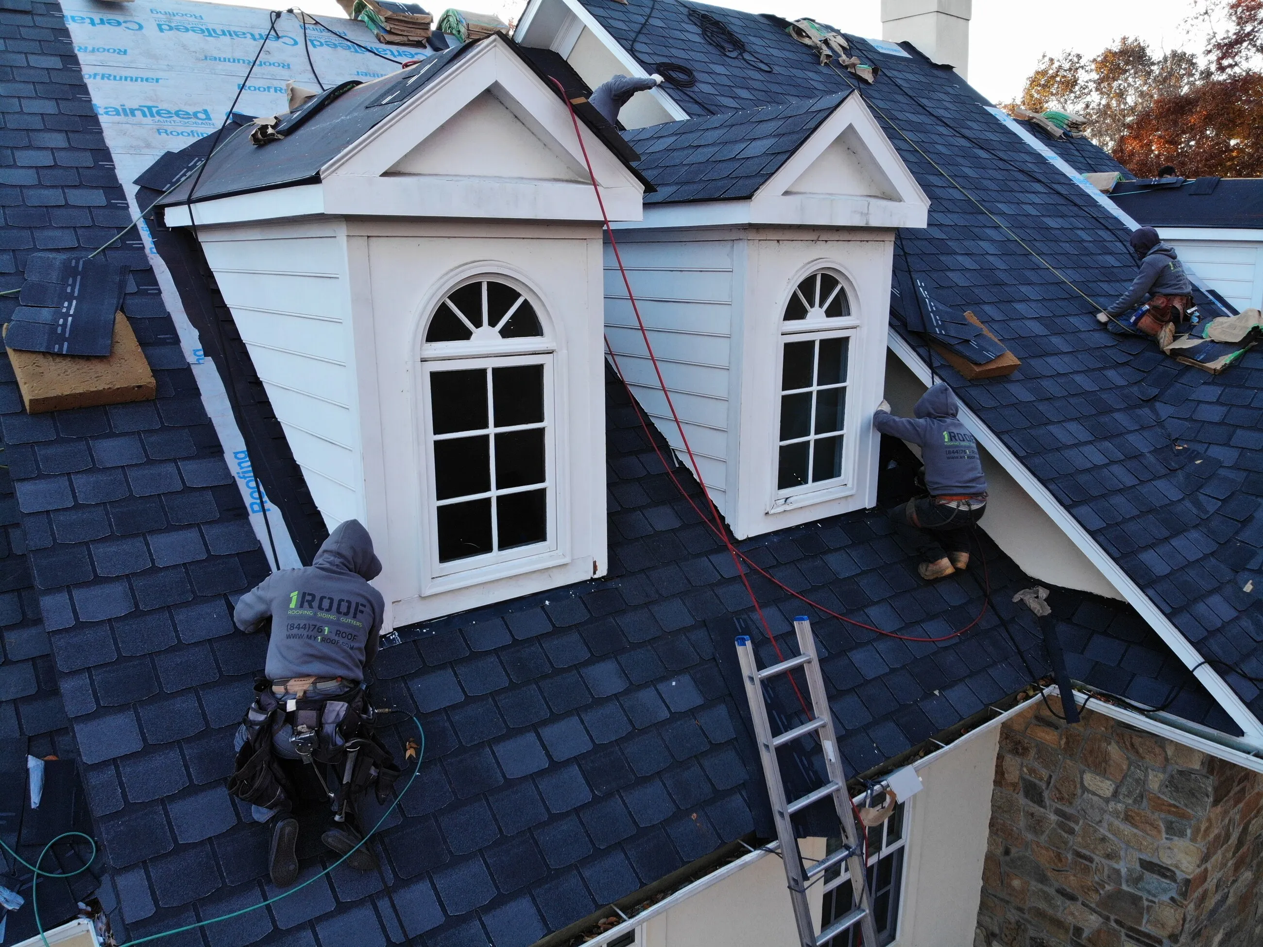 1ROOF crew installing slate-style shingles around arched-window dormers