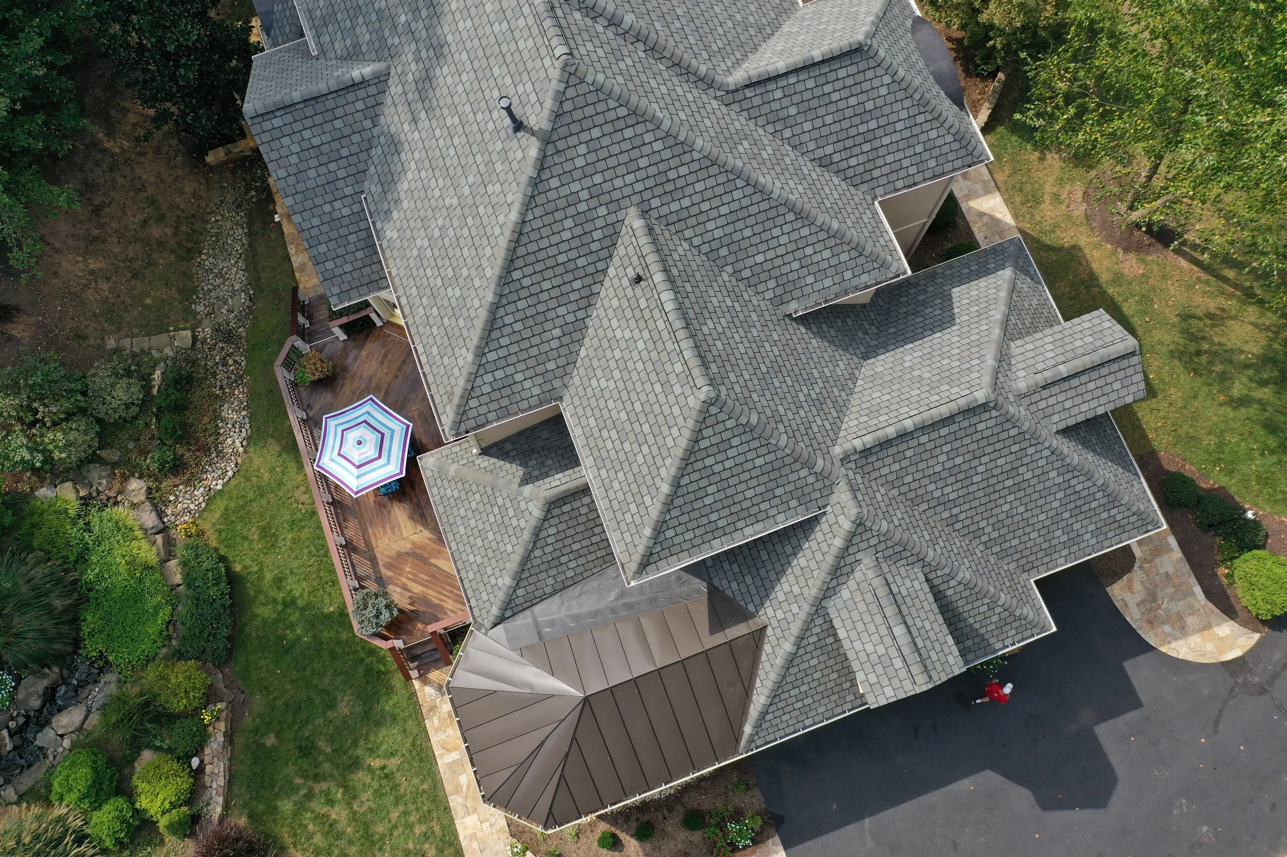 Top-down aerial of an estate roof with designer shingles and a bronze standing-seam bay window roof