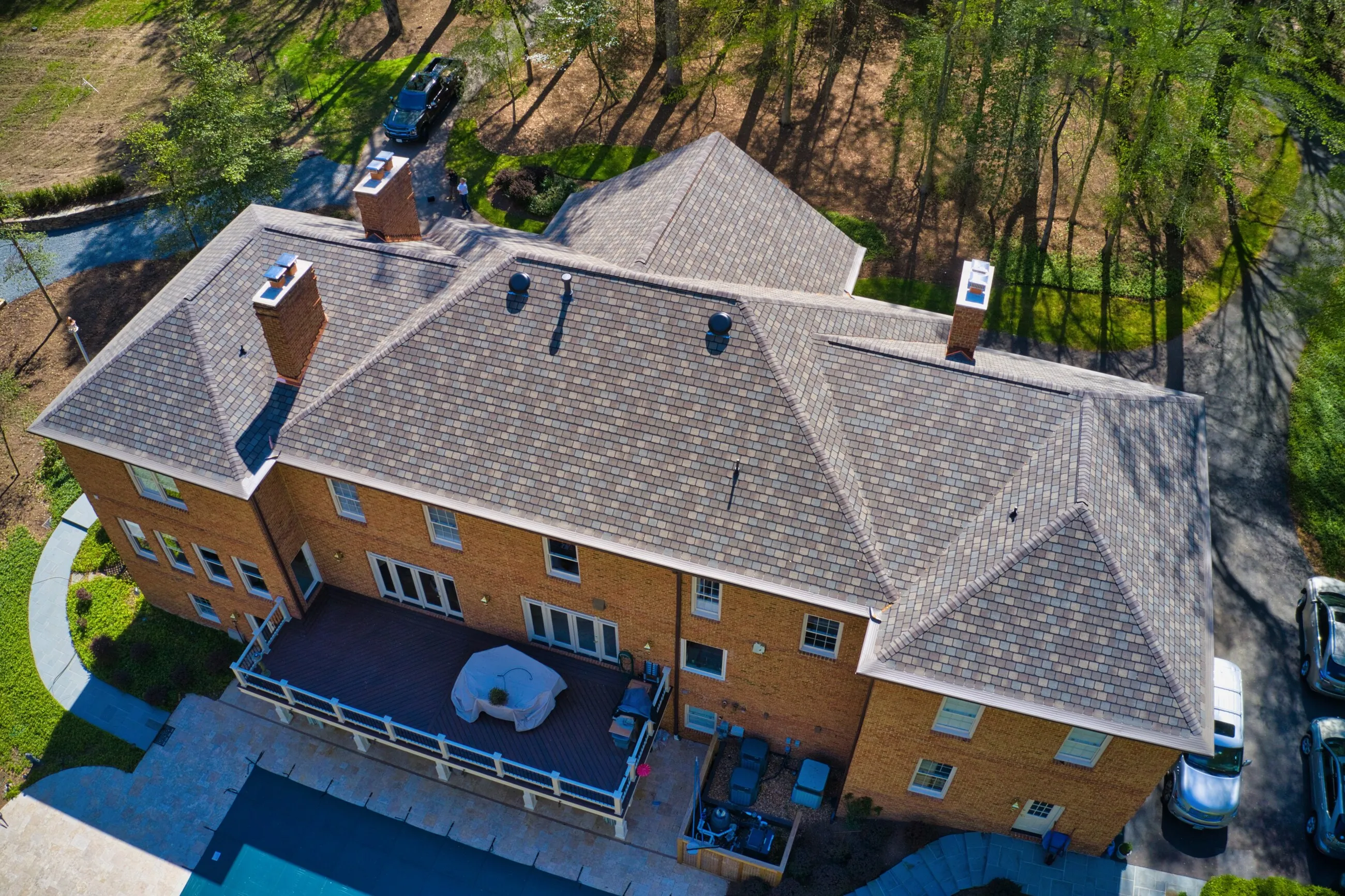 Aerial view of the rear of a brick estate with a new designer shingle roof above the pool deck
