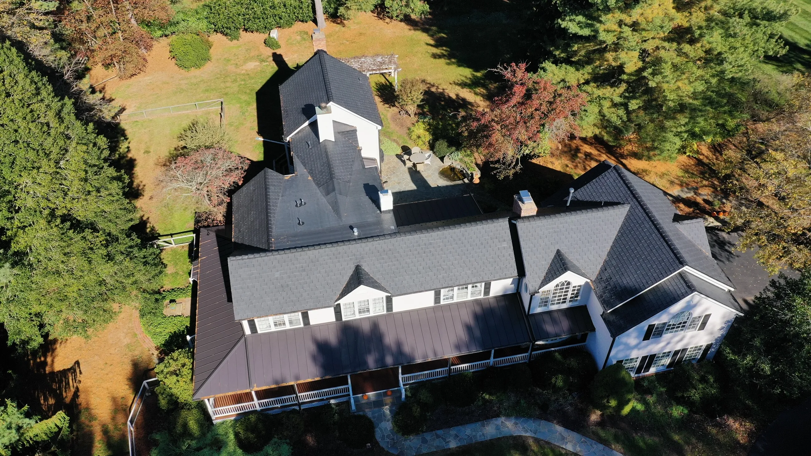Aerial view of a farmhouse with a new slate-style roof and standing-seam metal porch roof