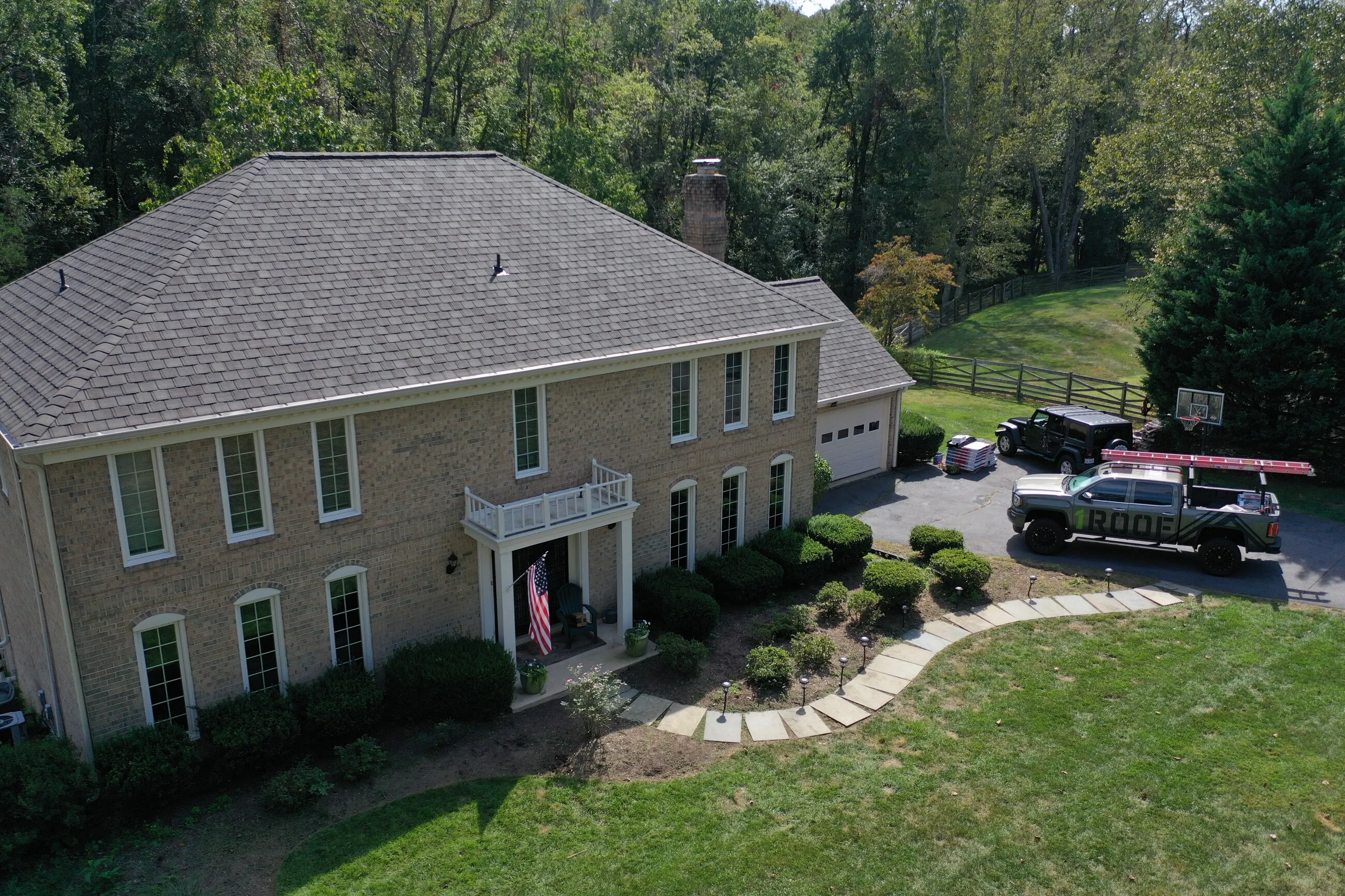Aerial view of a painted brick colonial with a new hip roof and a 1ROOF truck in the driveway