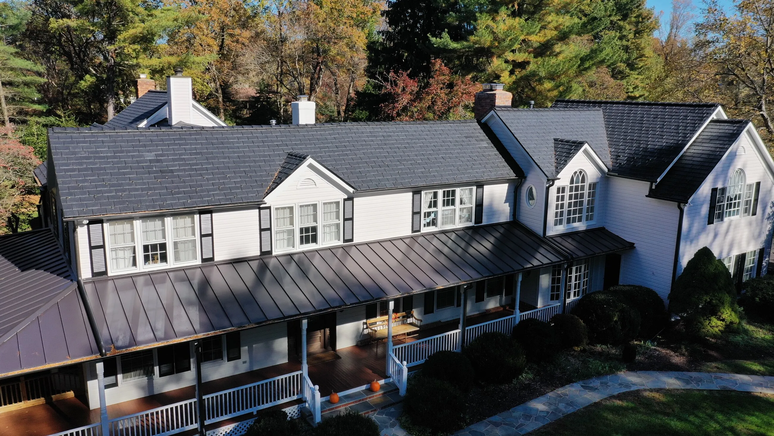 White farmhouse with a standing-seam metal porch roof and slate-style main roof