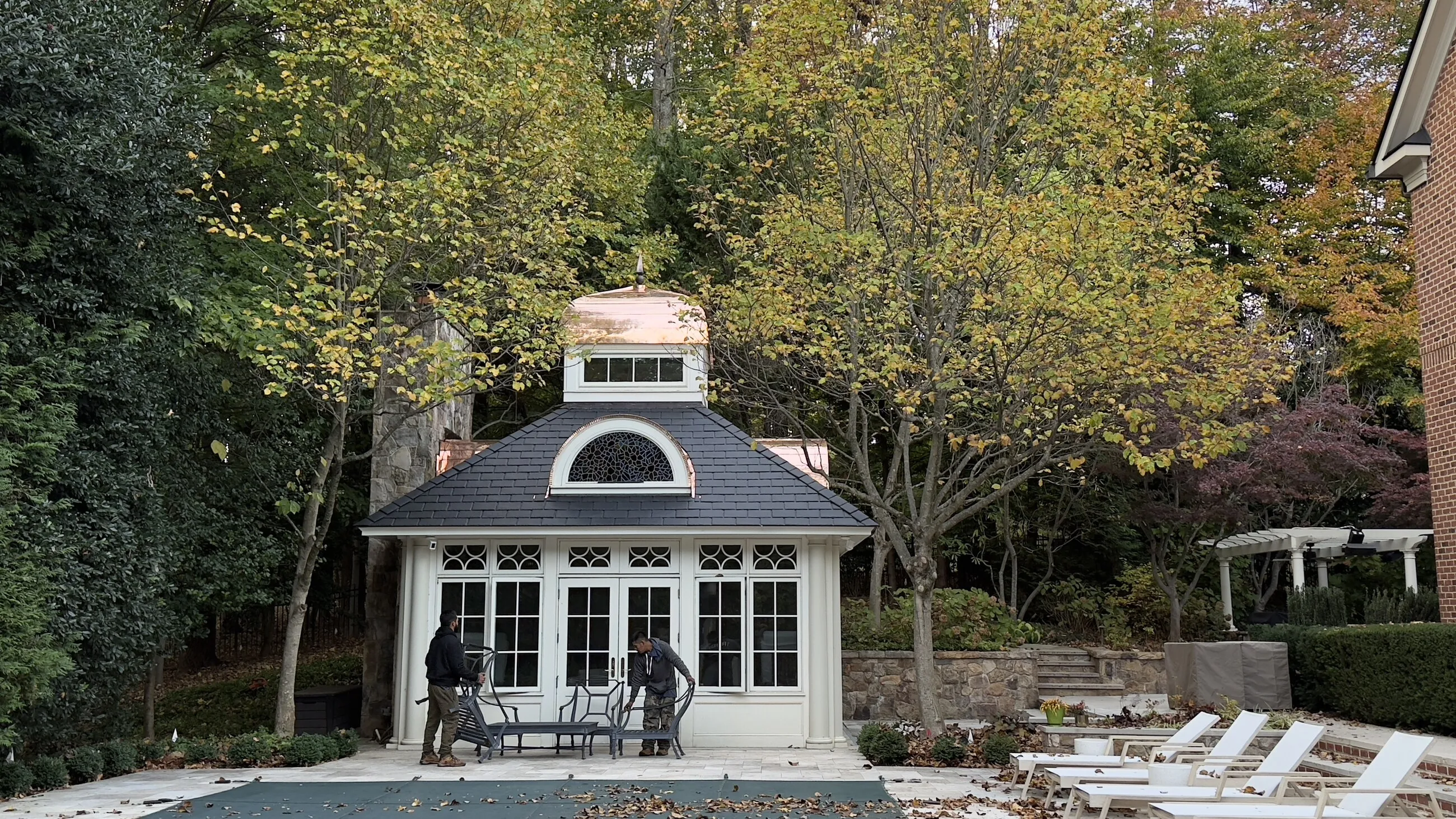 Pool house with an arched window and a copper-capped cupola beside a stone chimney