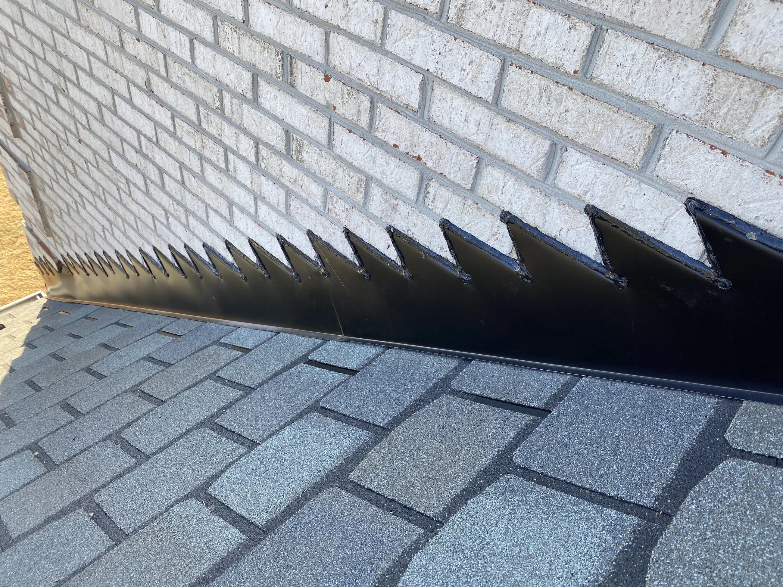 Custom sawtooth metal flashing where slate-style shingles meet a white brick wall