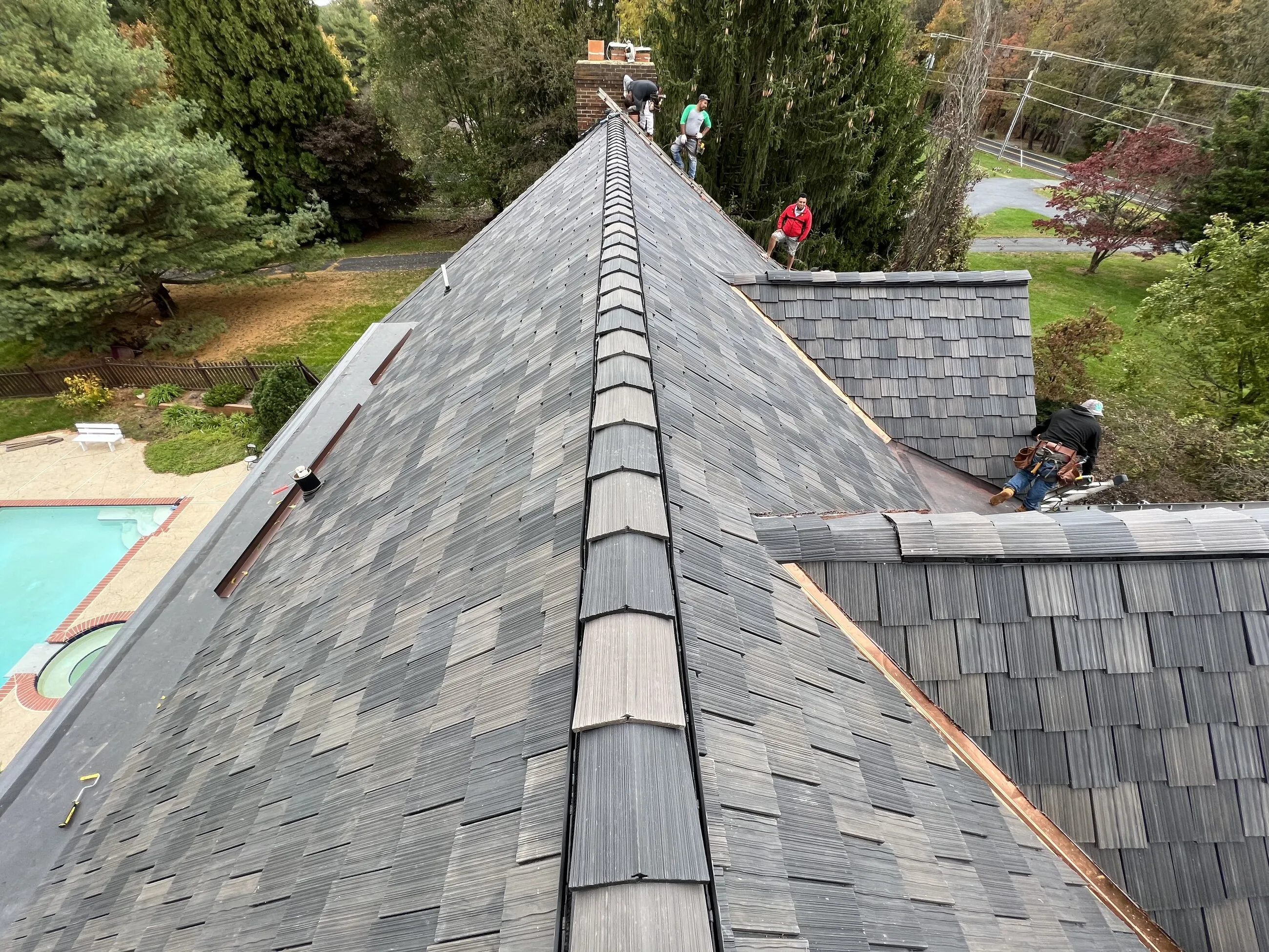View along a shake-style ridge with the 1ROOF crew working near a backyard pool