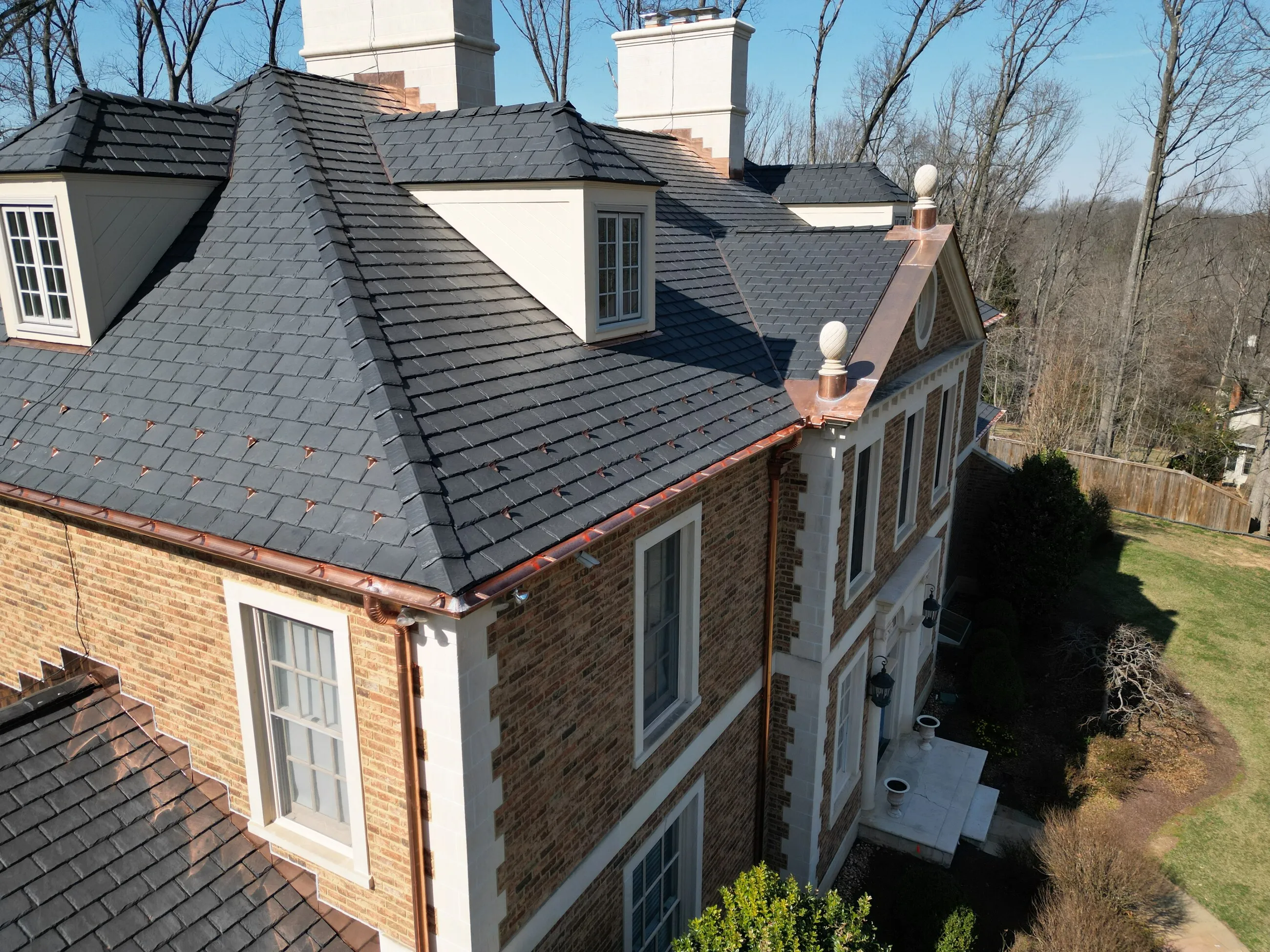 Slate roof with copper finials and a copper-topped bay on a stone manor