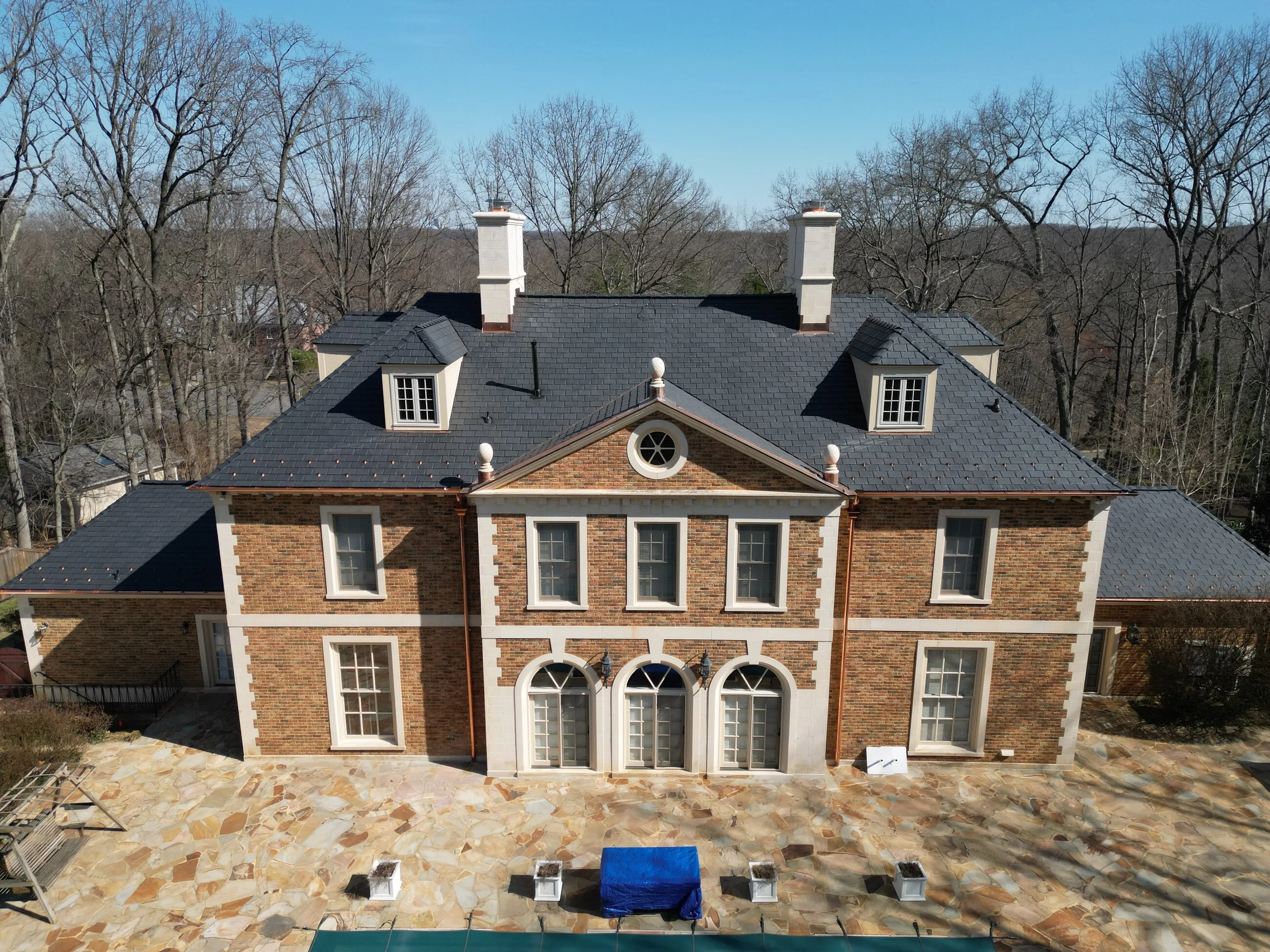 Stone manor home after asbestos slate removal with a new slate-style roof and copper accents