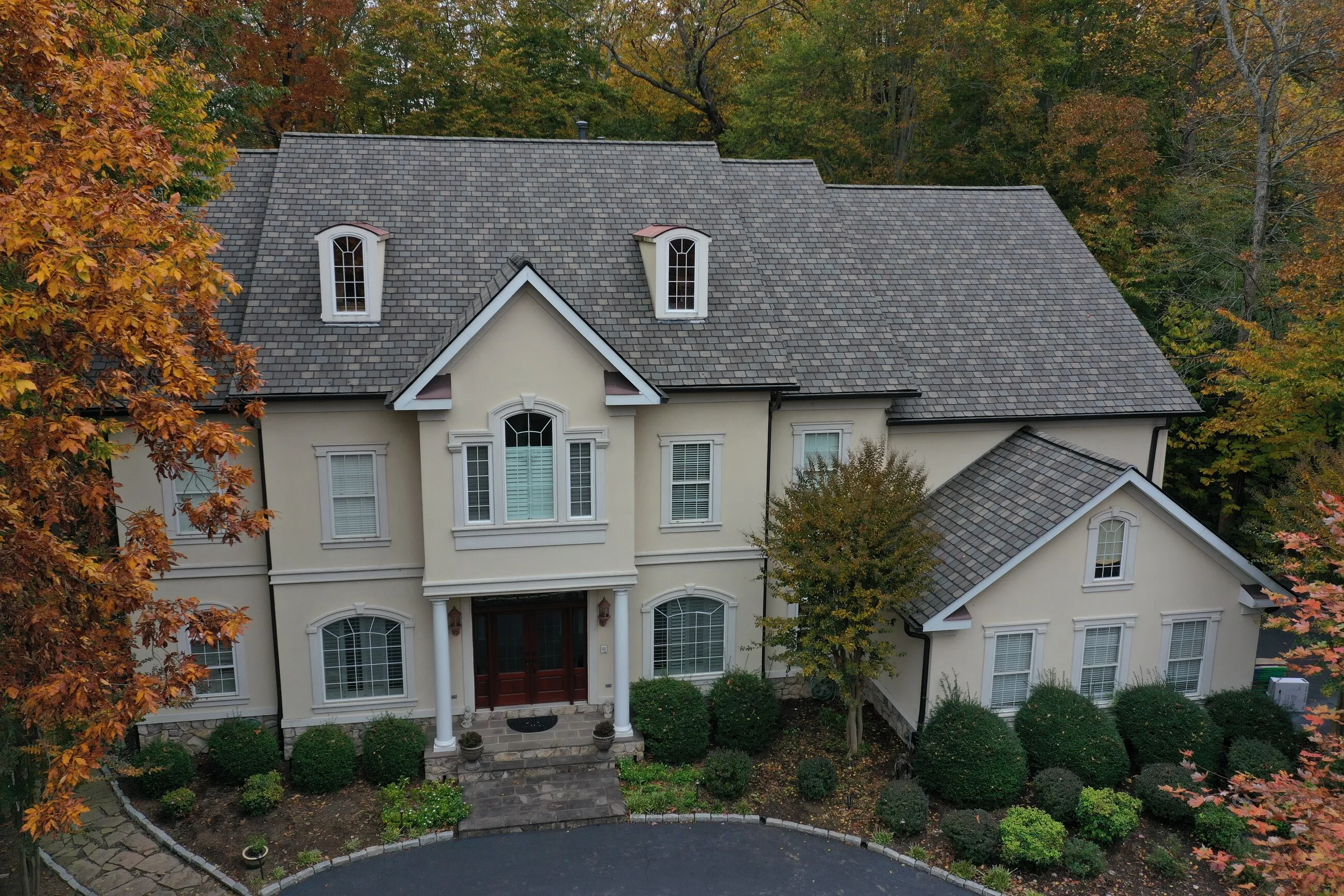 Stucco estate home with a new designer shingle roof surrounded by fall foliage