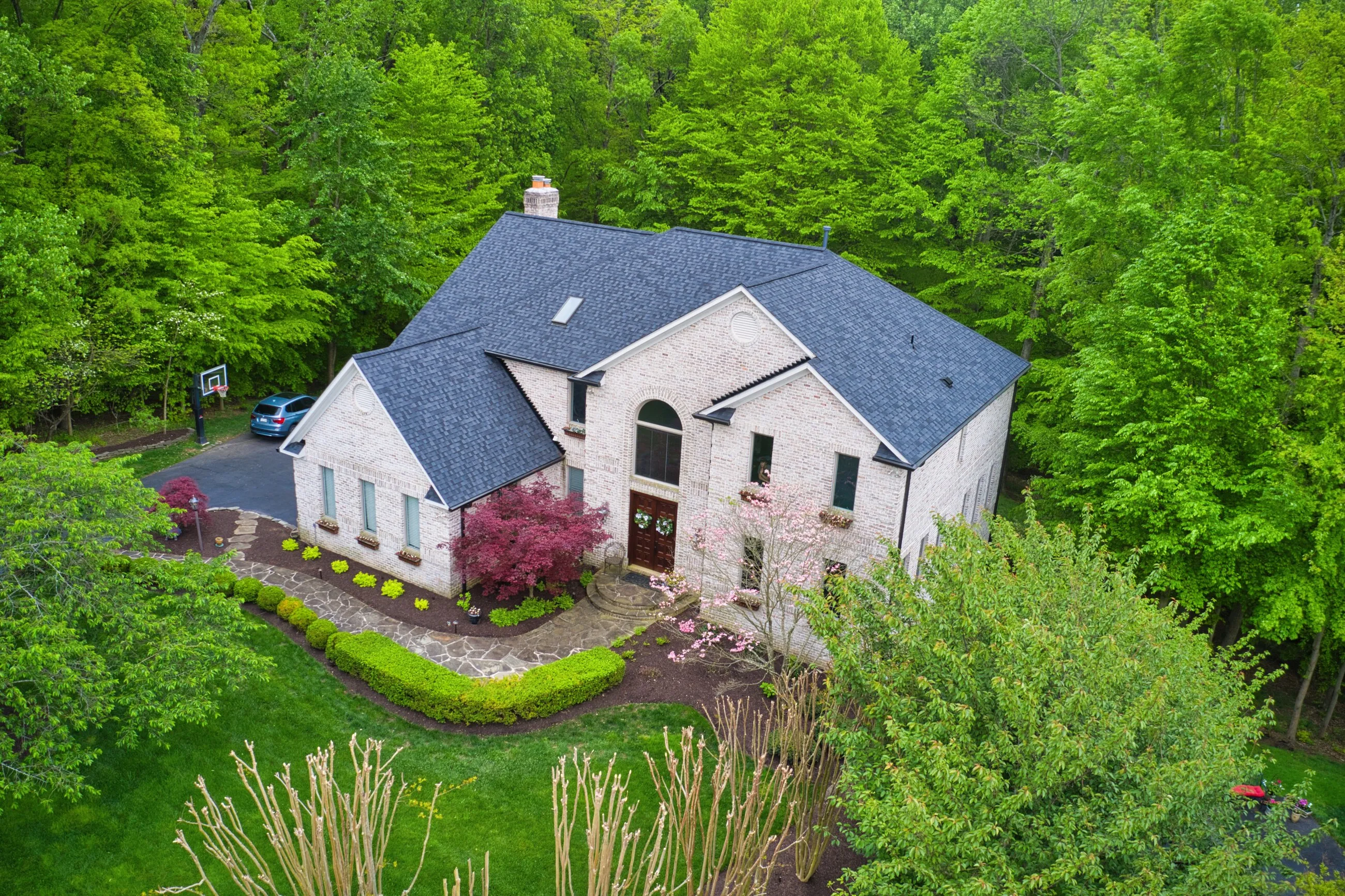 Aerial view of a stucco and stone manor with a new architectural shingle roof and manicured lawn
