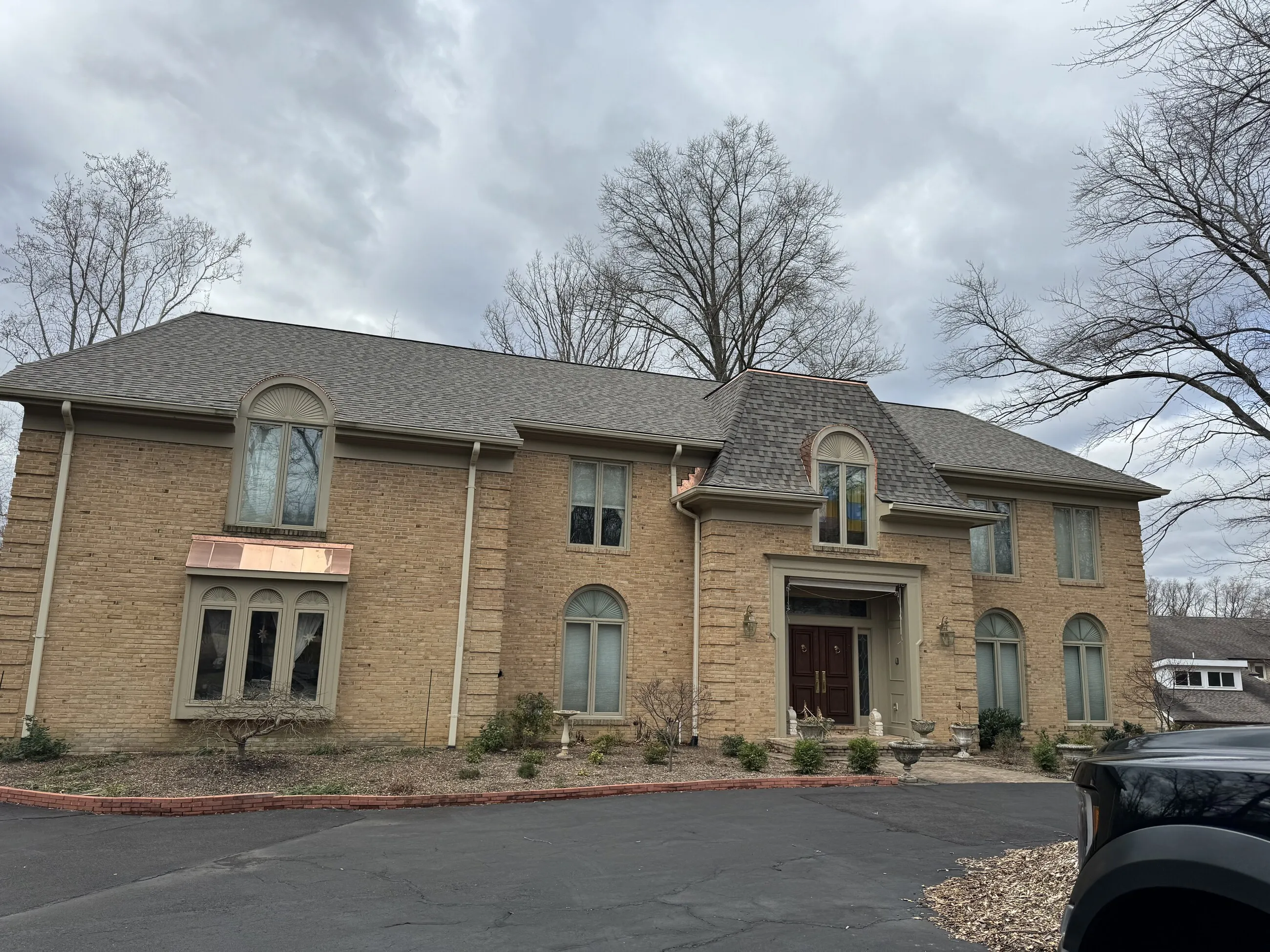 Tan brick manor with a new architectural shingle roof and copper bay window accents