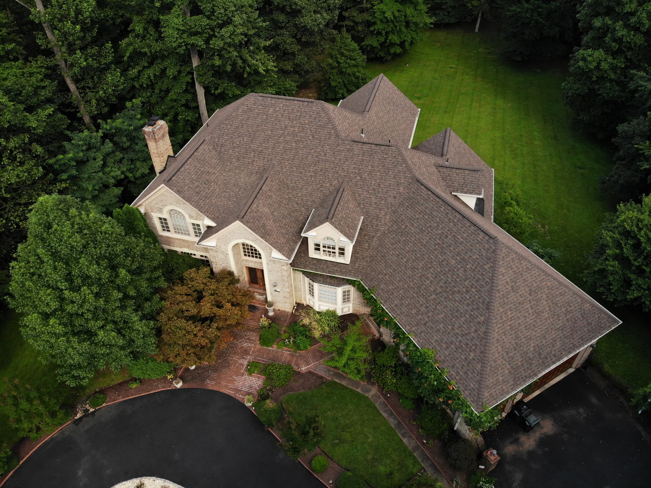 Aerial view of a hip-roof estate home with a new wood-tone designer shingle roof