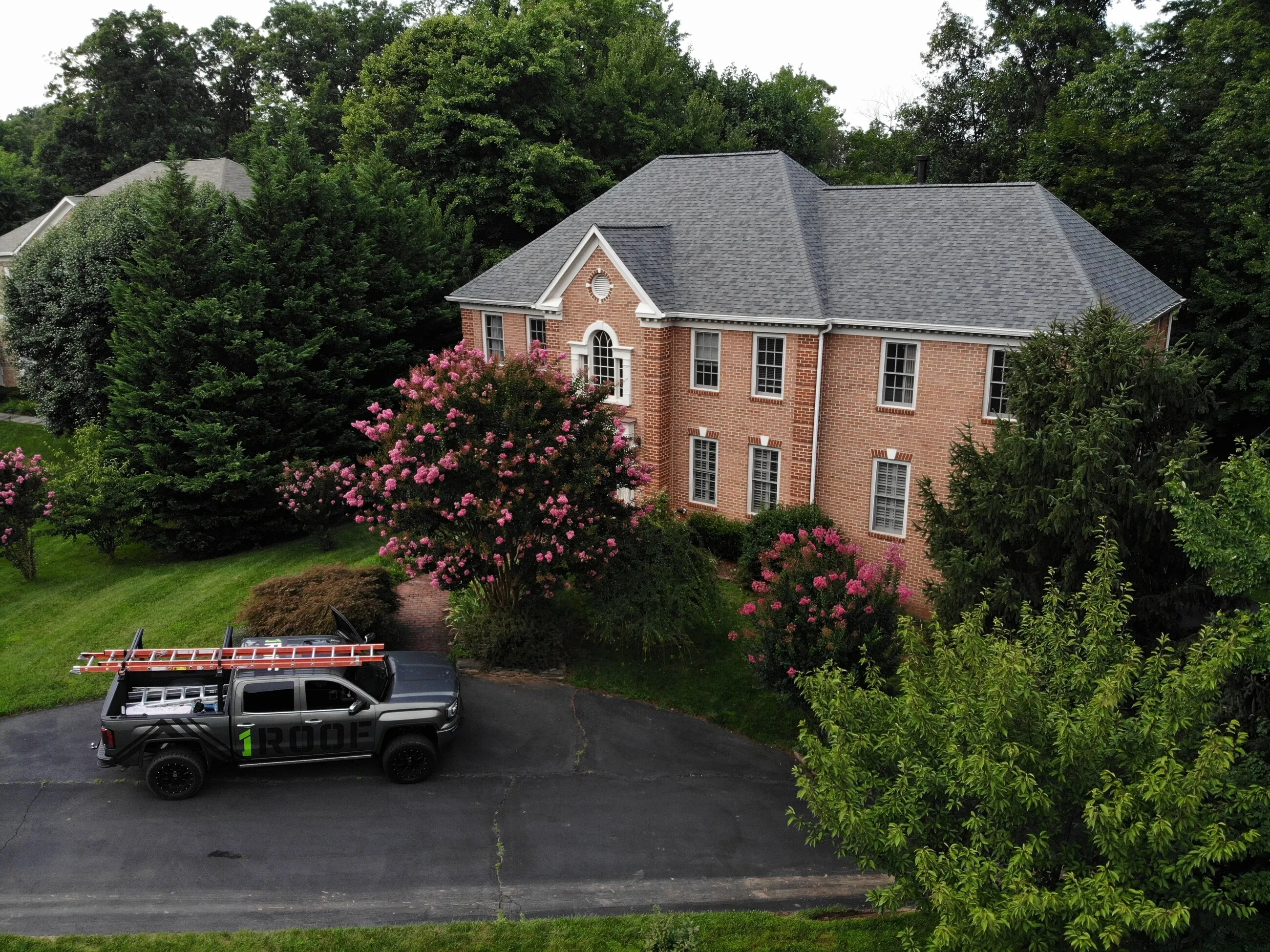1ROOF truck parked in front of a brick colonial home during a roofing project