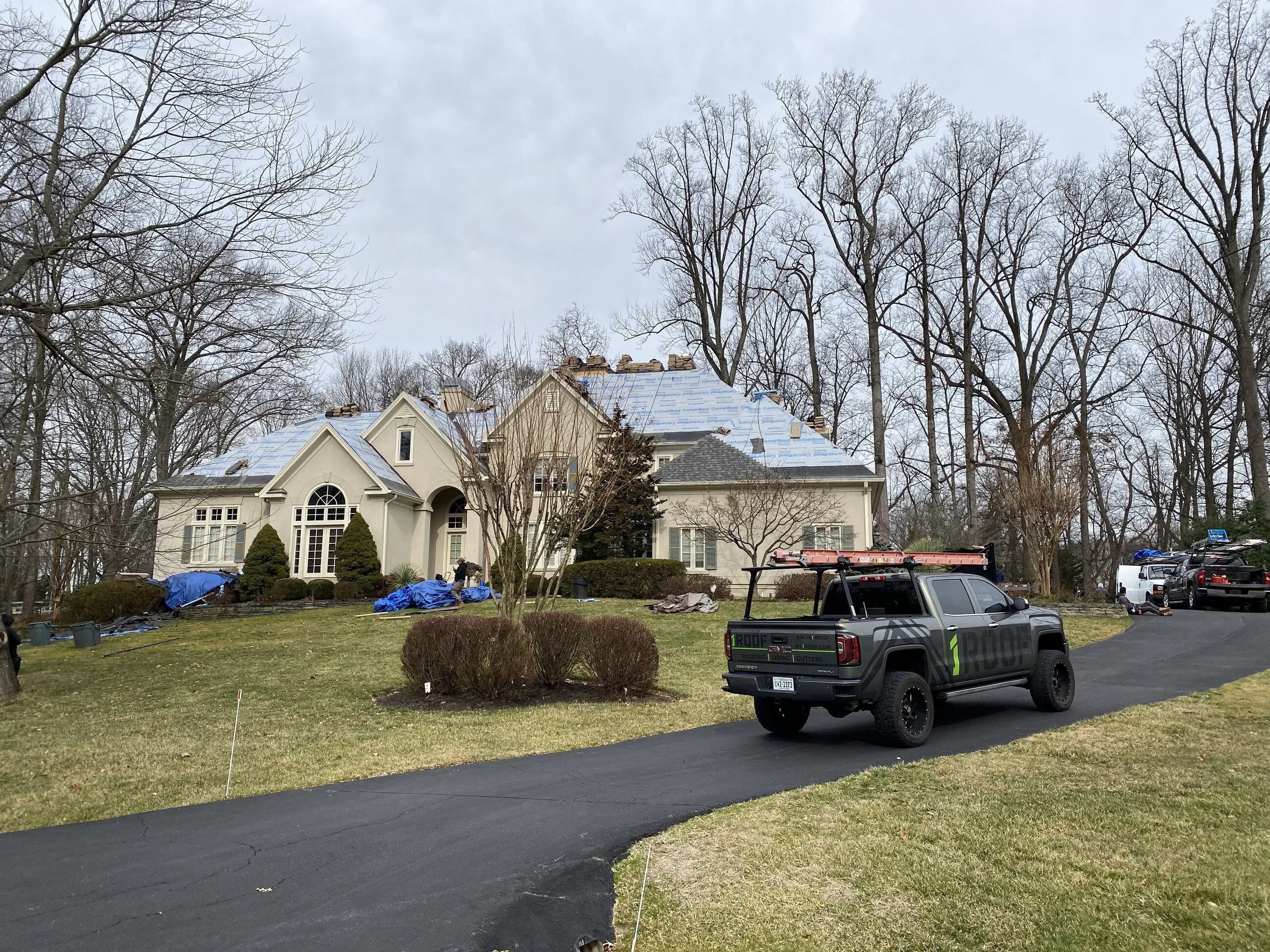 1ROOF truck in the driveway of a stucco estate during a roof replacement
