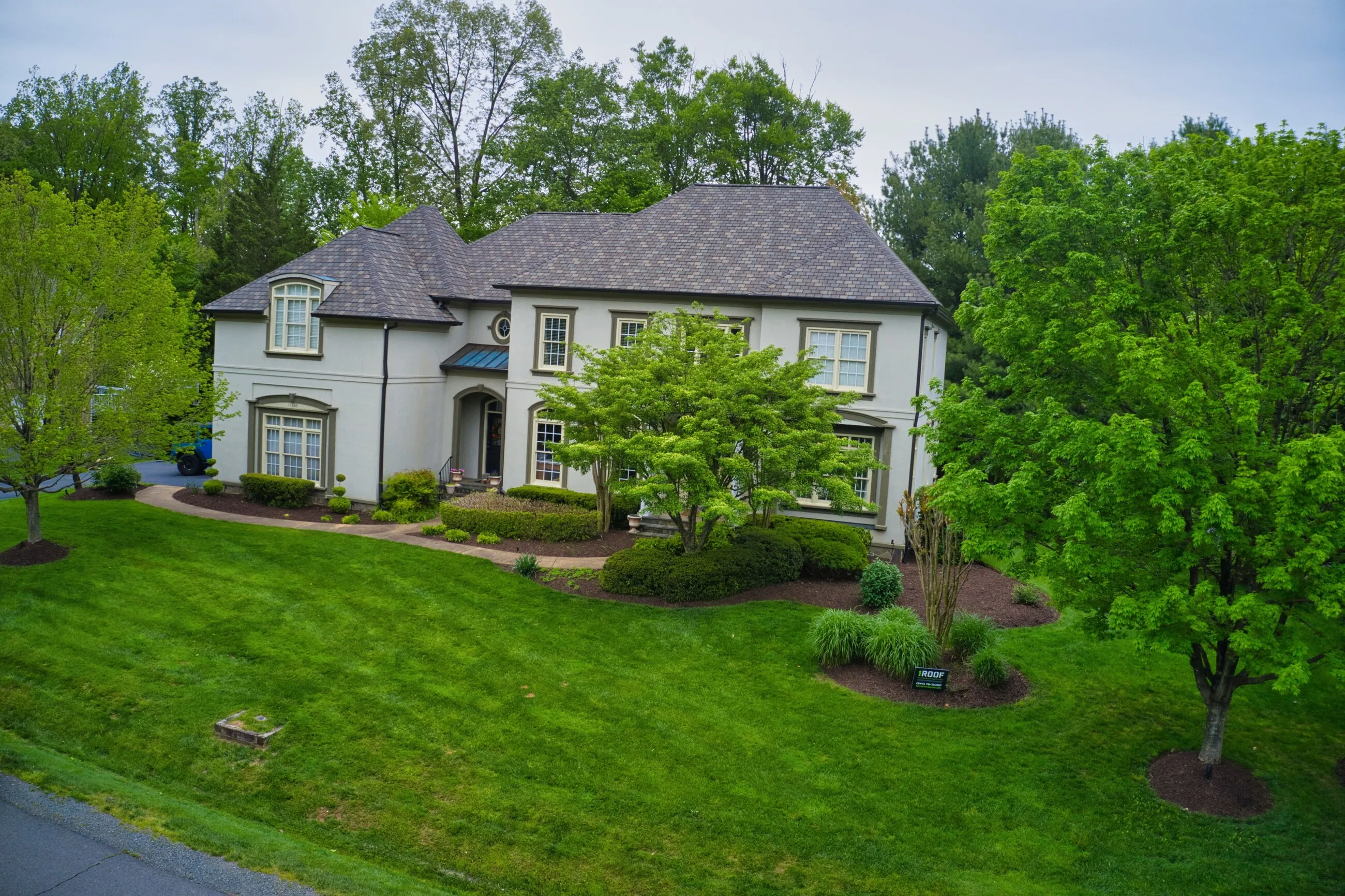Aerial view of a white brick home with a new architectural shingle roof in spring