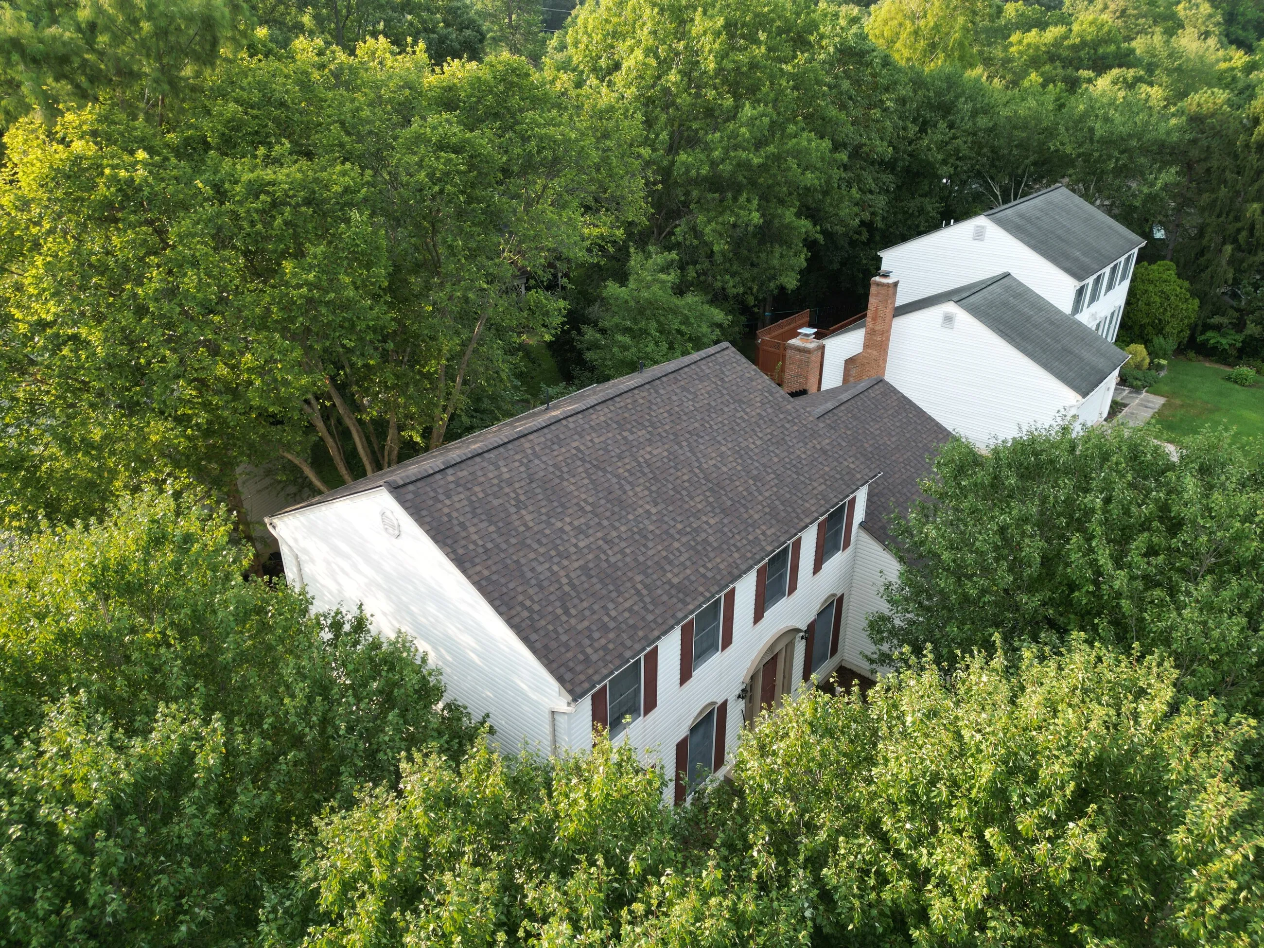 Aerial view of a white colonial with a new shingle roof among mature trees